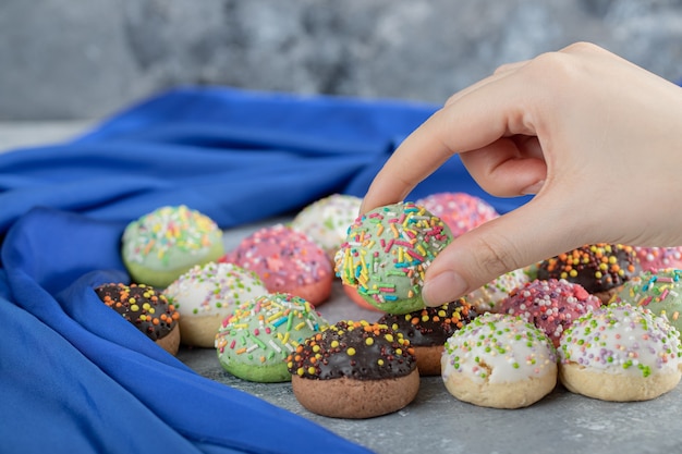 Weibliche Hand, die Glasurplätzchen auf Marmortisch nimmt.