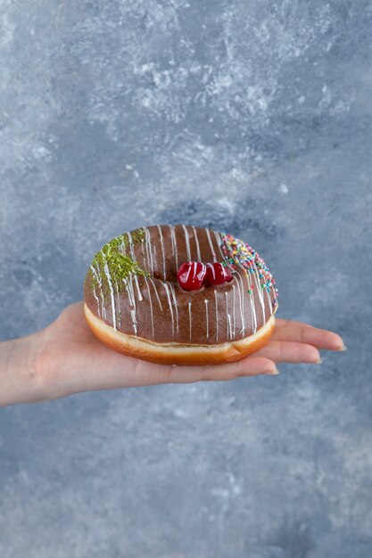 Weibliche Hand, die köstlichen Schokostreusel Donut auf Marmoroberfläche hält.