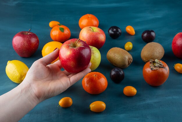 Weibliche Hand, die roten Apfel auf blauer Oberfläche hält.