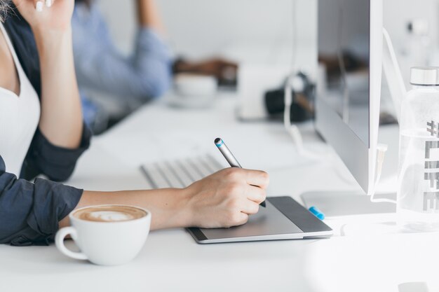 Weibliche Hand, die Stift auf Tablette hält. Innenporträt eines freiberuflichen Webentwicklers, der während der Kaffeepause im Büro an einem Projekt arbeitet.