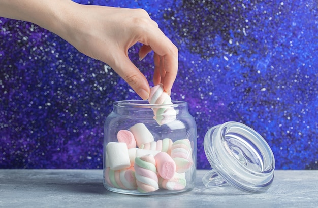 Weibliche Hand, die weiche bunte Marshmallows aus dem Glas nimmt