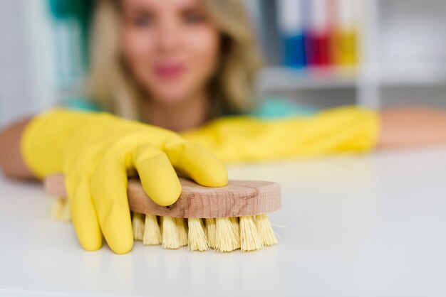 Weibliche Hand, die weißen Schreibtisch mit hölzerner Bürste säubert