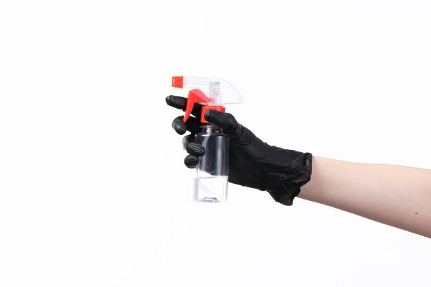 Weibliche Hand einer Vorderansicht im schwarzen Handschuh, der Spray auf Weiß hält