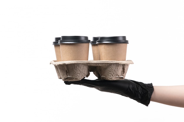Weibliche Hand einer Vorderansicht in schwarzen Handschuhen, die Tassen mit Kaffee auf weißem Job halten