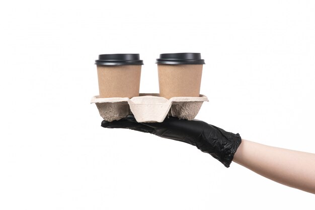 Weibliche Hand einer Vorderansicht mit schwarzen Handschuhen, die Kaffeetassen auf Weiß halten