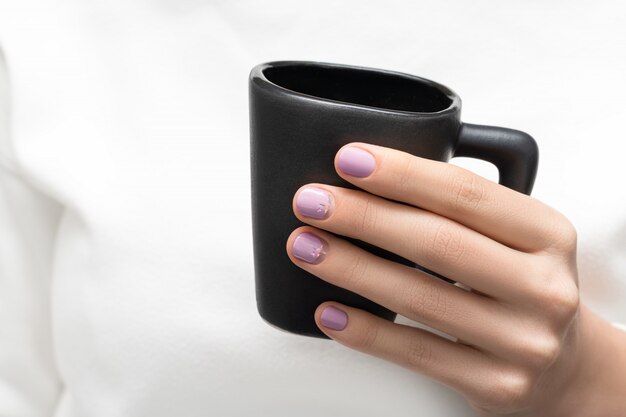 Weibliche Hand mit lila Nageldesign, das schwarze Kaffeetasse hält
