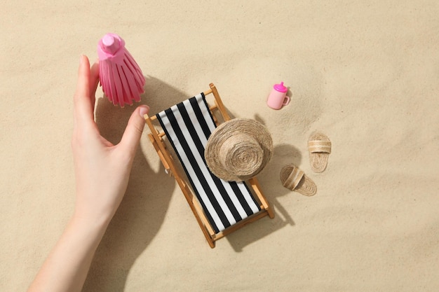 Weibliche Hand und Mini-Strandzubehör auf Sandhintergrund