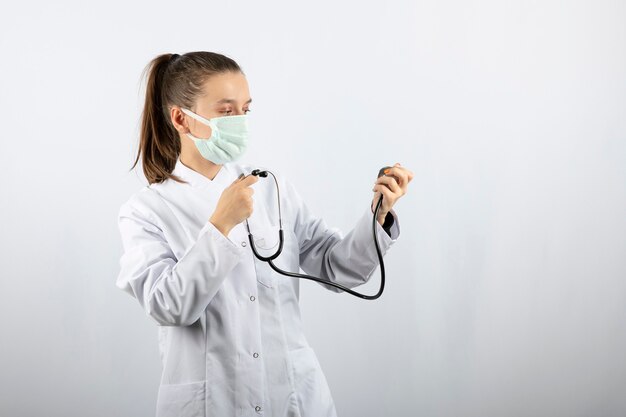 Weibliche junge Ärztin in weißer Uniform mit Blick auf ein Stethoskop