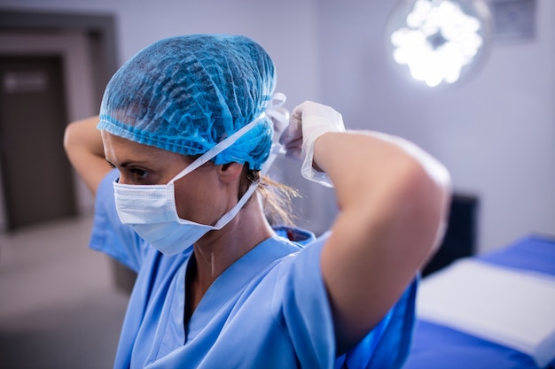 Weibliche krankenschwester, die chirurgische maske im operationssaal bindet