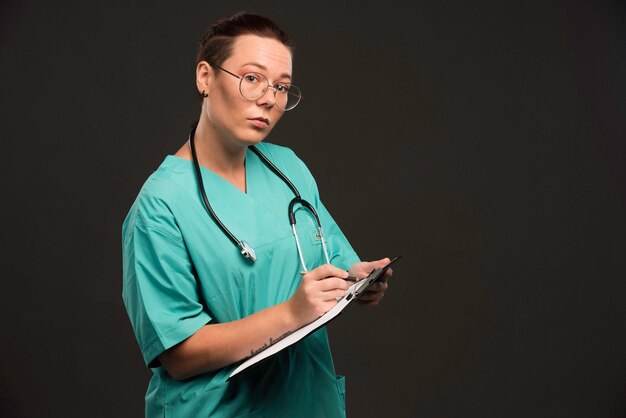 Weibliche Krankenschwester in der grünen Uniform, die den Rohling hält und Geschichte schreibt.