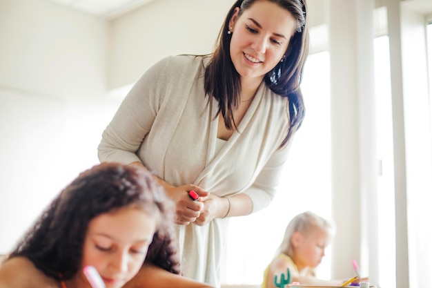 Weibliche Lehrerin lehnt über Schulmädchen