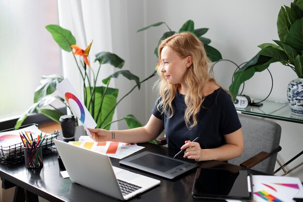 Weibliche Logo-Designerin, die an ihrem Tablet arbeitet, das mit einem Laptop verbunden ist