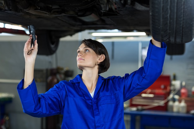 Weibliche Mechaniker ein Auto mit Taschenlampe Prüfung