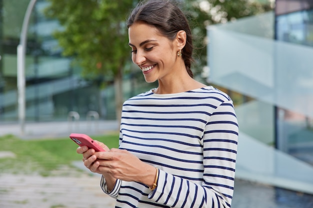weibliche Reisende verwendet App und GPS sucht nach Richtungstexten, während sie in der Stadt spazieren geht, trägt lässige Kleidung Nachrichten mit Freundposen draußen allein liest positives Feedback unter Post