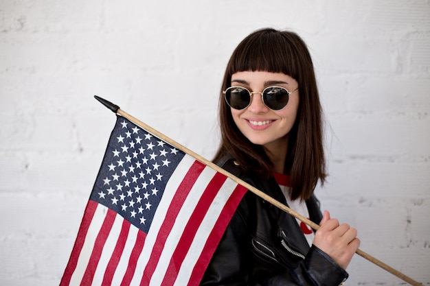 Weibliche schöne Frau oder Teenager-Mädchen trägt neue Sonnenbrillenbrille vor amerikanischer Flagge, trendiger und modischer Hipster, Patriot der USA