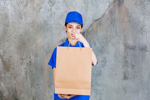 Weibliche Servicemitarbeiterin in blauer Uniform, die eine Einkaufstasche aus Pappe hält und sie dem Kunden gibt.