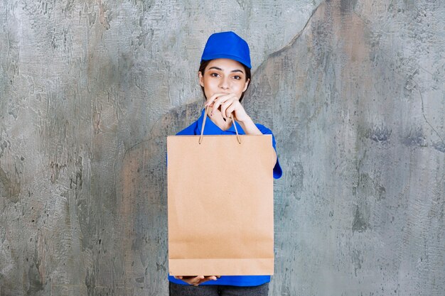 Weibliche Servicemitarbeiterin in blauer Uniform, die eine Papiertüte hält und dem Kunden übergibt.