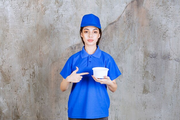 Weibliche Servicemitarbeiterin in blauer Uniform, die eine Plastikschüssel hält