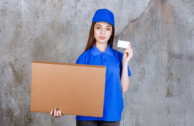 Weibliche Servicemitarbeiterin in blauer Uniform, die einen Karton hält und ihre Visitenkarte vorlegt