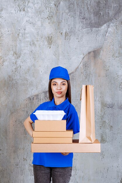 Weibliche Servicemitarbeiterin in blauer Uniform, die Kartons, Taschen und Kisten zum Mitnehmen hält.