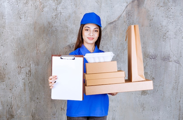Kostenloses Foto weibliche servicemitarbeiterin in blauer uniform, die kartons, tüten und kisten zum mitnehmen hält und die unterschriftenliste vorlegt.