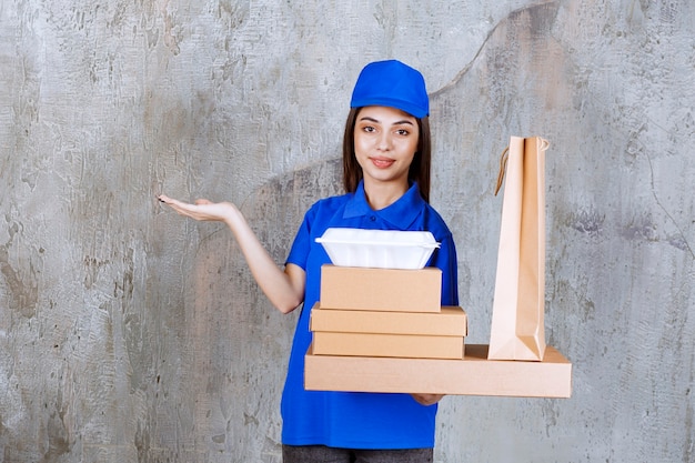 Weibliche Servicemitarbeiterin in blauer Uniform mit Pappkartons, Einkaufsbox und Takeaway-Boxen