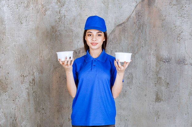 Weibliche Servicemitarbeiterin in blauer Uniform mit zwei Plastikbechern.