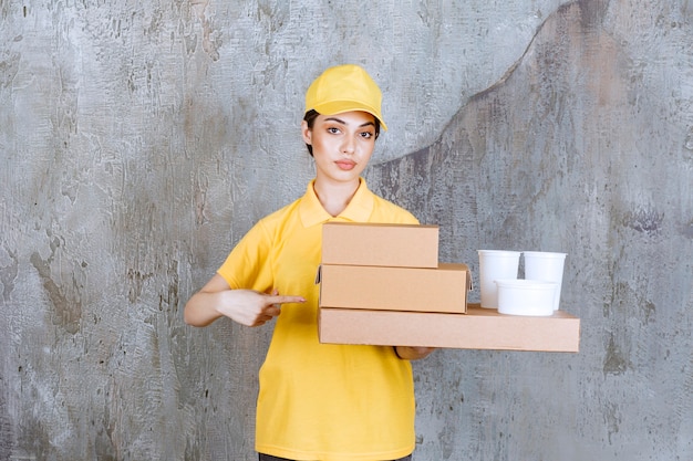 Kostenloses Foto weibliche servicemitarbeiterin in gelber uniform, die einen vorrat an pappkartons und plastikbechern zum mitnehmen hält