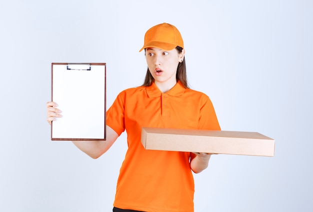 Weibliche Servicemitarbeiterin in orangefarbenem Dresscode, die eine Pizzaschachtel zum Mitnehmen aus Pappe hält und um Unterschrift bittet, während sie verwirrt aussieht