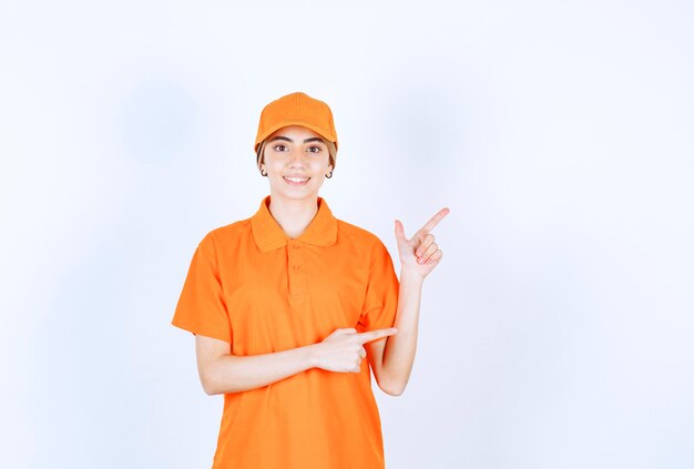 Weibliche Servicemitarbeiterin in orangefarbener Uniform, die auf etwas beiseite zeigt