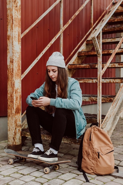 Weibliche Skaterin, die neben ihrem Skateboarding draußen sitzt