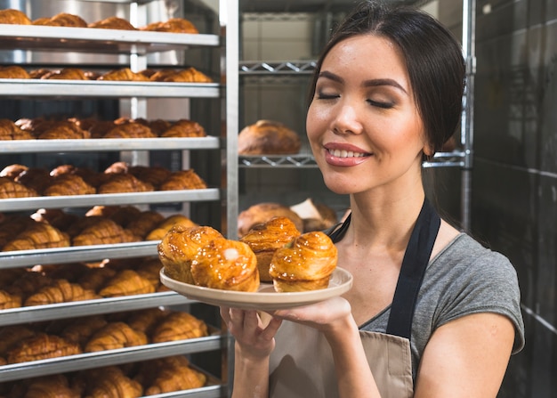 Weiblicher bäcker in der bäckerei, die frischen blätterteig auf platte riecht