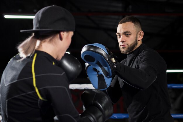 Weiblicher Boxer mit Schutzhandschuhen übend mit Trainer