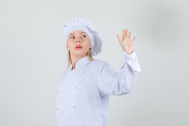 Kostenloses Foto weiblicher chef, der hand winkt, während in weißer uniform zurückblickt.