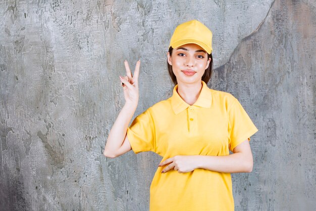 Weiblicher Dienstagent in der gelben Uniform, die auf Betonwand steht und Frieden schickt.