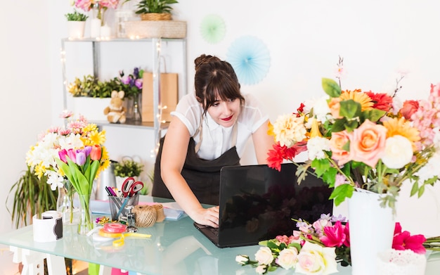 Weiblicher Florist, der an Laptop mit Blumen auf Schreibtisch arbeitet