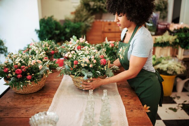 Weiblicher Florist, der Korb von Blumen auf hölzernem Schreibtisch vereinbart