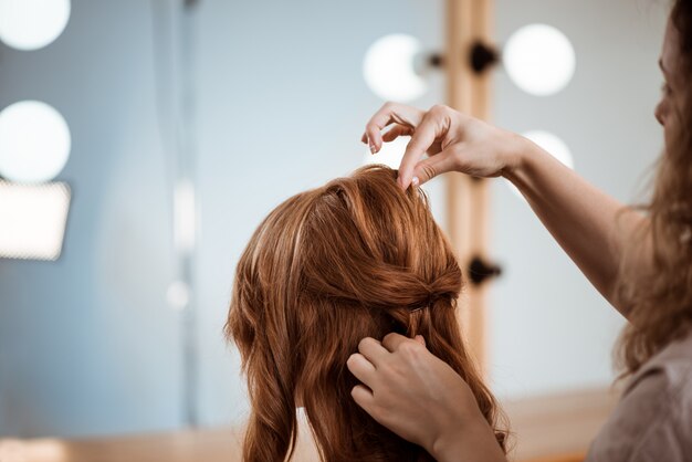 Weiblicher Friseur, der Frisur zu rothaariger Frau im Schönheitssalon macht