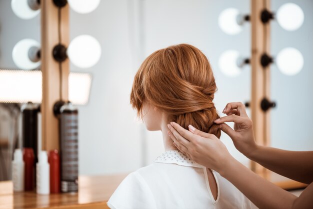 Weiblicher Friseur, der Frisur zu rothaariger Frau im Schönheitssalon macht