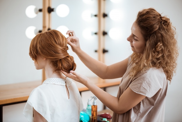 Weiblicher Friseur, der Frisur zu rothaariger Frau im Schönheitssalon macht