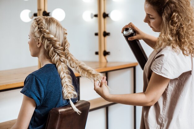 Weiblicher Friseur, der Frisur zur blonden Frau im Schönheitssalon macht