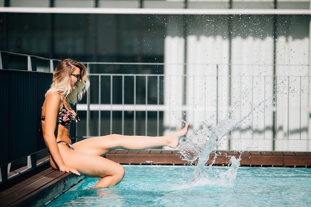 Weiblicher fuß im blauen wasser. füße plätschern im pool. frauenbeine spielen und tummeln sich mit wasser in einem schwimmbad.