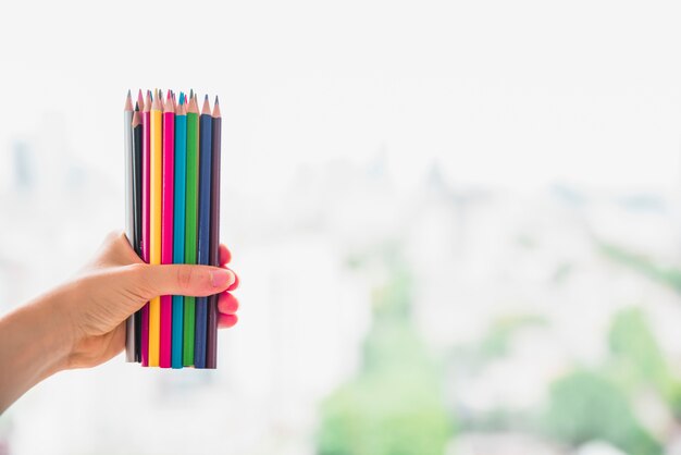 Weiblicher Handholding-Satz farbige Bleistifte gegen unscharfen Hintergrund