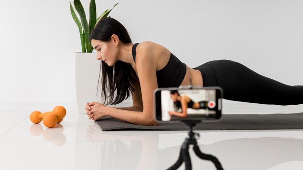 Weiblicher Influencer zu Hause Vlogging während des Trainings mit Smartphone