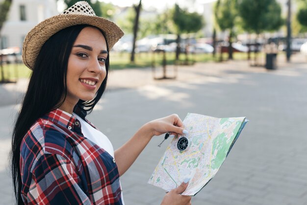 Weiblicher junger Reisender, der Navigationskompass und Karte beim Betrachten der Kamera hält