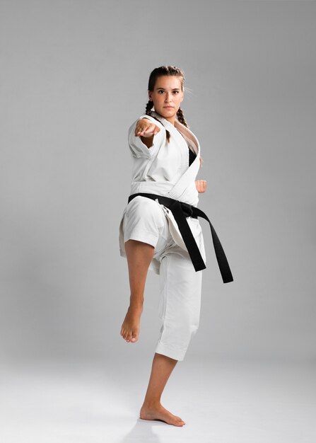 Weiblicher Karatekämpfer, der den Tritt lokalisiert auf grauem Hintergrund durchführt