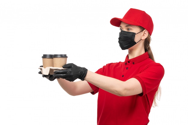 Weiblicher Kurier der Vorderansicht in den roten Handschuhen der roten Kappe des roten Hemdes und der schwarzen Maske, die Kaffee hält