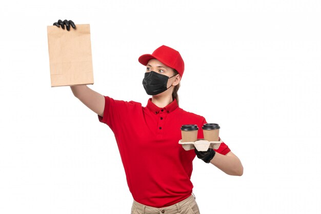 Weiblicher Kurier der Vorderansicht in den roten Handschuhen der roten Kappe des roten Hemdes und der schwarzen Maske, die Lebensmittelpaket und Kaffee auf Weiß hält
