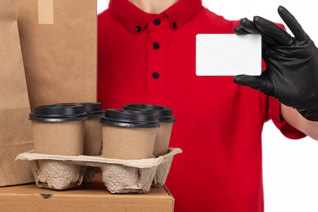 Weiblicher Kurier der Vorderansicht in den schwarzen Handschuhen des roten Hemdes, die Lebensmittelpaket und Kaffee halten