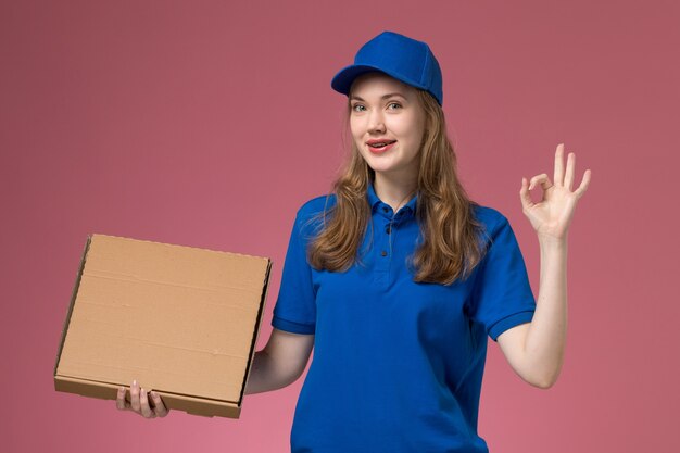 Weiblicher Kurier der Vorderansicht in der blauen Uniform, die Nahrungsmittelbox auf der rosa Hintergrundjobdienstuniformfirma hält
